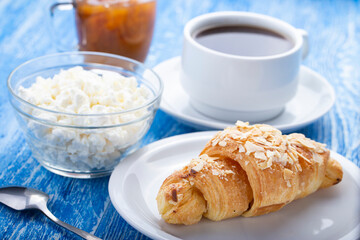 Morning breakfast. Fresh French croissant with coffee, jam and cottage cheese on a blue wooden surface.