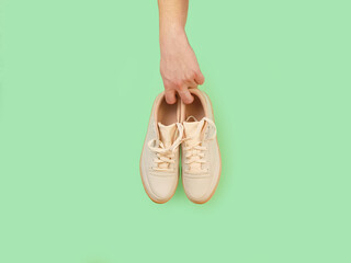 Male hand holds unbranded beige sneakers isolated on green background with copy space. Top view.