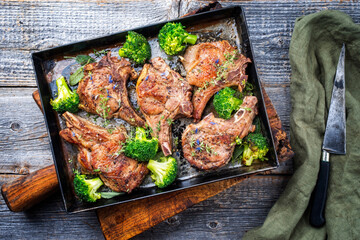 Traditional barbecue dry aged veal chops with baby broccoli served as close-up in a rustic tray on a wooden board - obrazy, fototapety, plakaty
