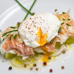 Poached egg on a bed of leek and marinated fresh salmon, chive sauce, on white plate