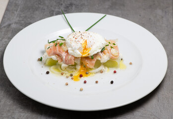 Poached egg on a bed of leek and marinated fresh salmon, chive sauce, on white plate