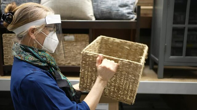 Mature woman wearing face shield and mask shopping for furniture in big box retail hardware store. Concept of safe shopping during pandemic.