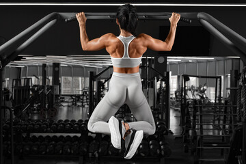 Athletic girl doing pull up exercise on horizontal bar. Fitness woman working out in gym