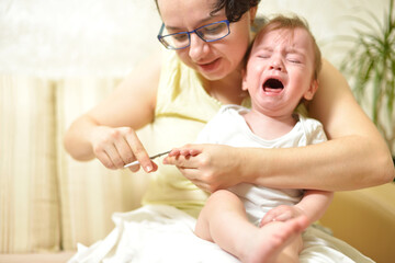 selective focus The mother cuts the child's toenails on the arm with baby safe scissors. Self care authentic concept. Mother care is most important for baby healthy life lifestyle. The baby is crying