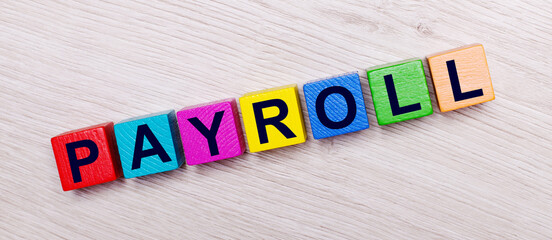 On a light wooden background on multi-colored bright wooden cubes the word PAYROLL