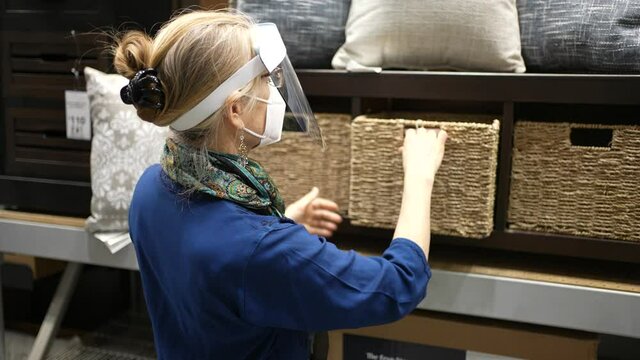 Mature woman wearing face shield and mask shopping for furniture in big box retail hardware store. Concept of safe shopping during pandemic.