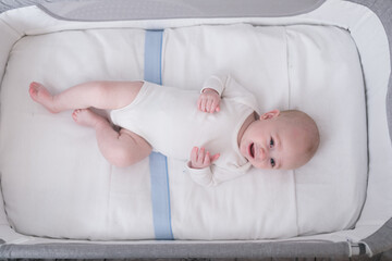 6 month old baby boy lying in his crib looking at the camera and smiling. baby products concept