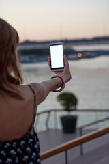 Young woman holding cellphone with blank white screen in urban city surroundings.