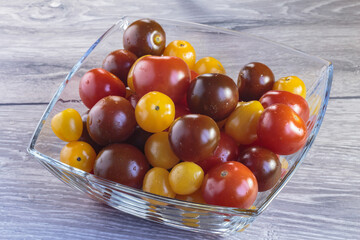 Multicolored tomatoes of different varieties in a glass bowl. Fashionable vegan food.