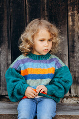 Fototapeta premium Portrait of a beautiful and happy curly girl in a knitted sweater near a wooden wall