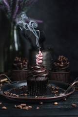 Several muffins or cupcakes with chocolate shaped cream at black table. Festive candle burns on a chocolate cake.