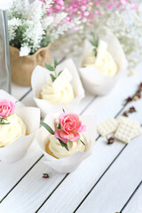 Several cupcakes and muffins with white butter cream and a lively pink rose on a white wooden table. Valentine's day or Mother's Day gift. Fresh flowers are on the table nearby. Rustic style.
