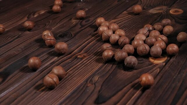 Close-up of macadamia nuts scattered on a wooden brown background.