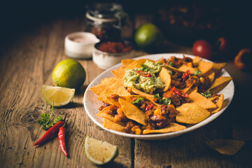 Delicious plate of yellow corn nachos chips with cheese, minced meat and red hot spicy salsa over wooden table