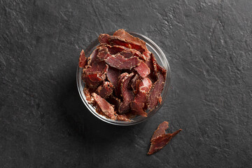 Bowl with jerky meat on a dark background, top view