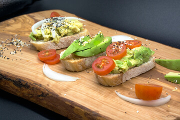 Variety of sandwiches for breakfast, appetizers with seeds and tomatoes on wooden board, dark background. Avocado sandwiches. Food photo, healthy food.