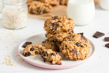 Chocolate oat cookies served on a white plate, oats and a glass of milk in the background