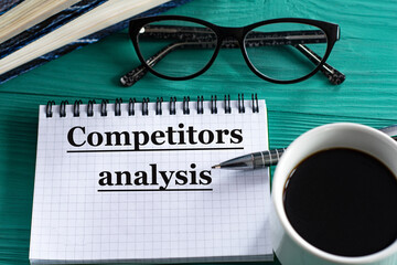COMPETITORS ANALYSIS - words in a notepad on a wooden green background with a calculator, pen and glasses
