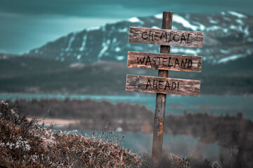 chemical wasteland ahead text quote engraved on wooden signpost outdoors in landscape looking polluted and apocalyptic.