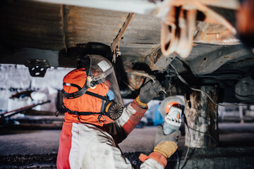 car body work, the master cleans the bottom of the truck with a grinder