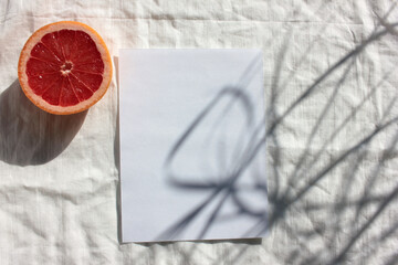 Summer still life with half of grapefruit and blank paper card on white fabric background....