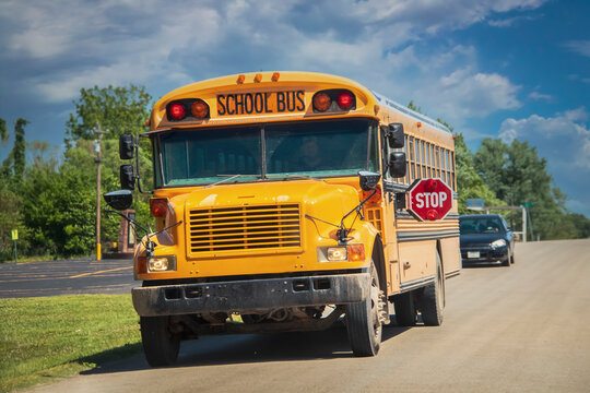 USA Yellow School Bus Stopping On Rural Road With Car Stopped Behind It.