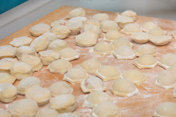 Lots of homemade dumplings on table with flour. Raw ravioli are ready for cooking. Close-up, selective focus