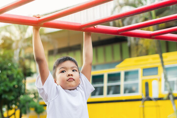 Obraz premium Kid exercise for health and sport concept. Happy Asian student​ child boy playing and hanging from a steel bar at the playground. 6-7 years old.