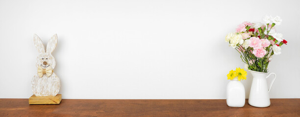 Rustic wood Easter bunny decor and spring flowers on a wood shelf against a white wall banner. Copy space.