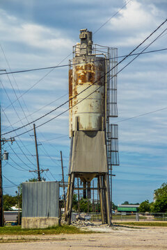 Old grungy rusty Silo for Concrete Batching Plant standing against blue cloudy sky with many electrical highlines near Cushing USA.