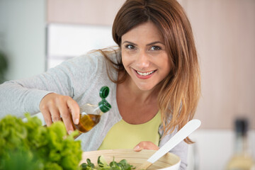 young woman pouring olive oil in to the salad