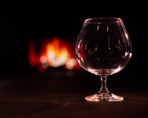 Empty brandy glass on the background of the fireplace in the dark.