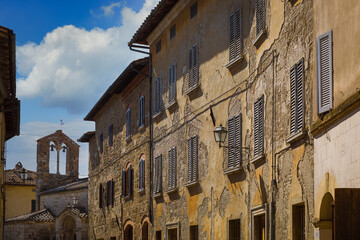 Fototapeta na wymiar Medieval buildings along the main street with the church of Santa Maria Assunta, San Quirico d'Orcia, Italy