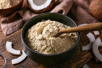 Bowl with coconut flour and spoon on wooden background