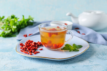 Cup with goji tea on color background