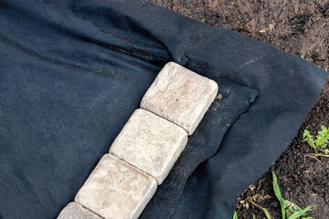 Edging of a laid woven geotextile fabric with sandstone pavers in the summer garden under reconstruction