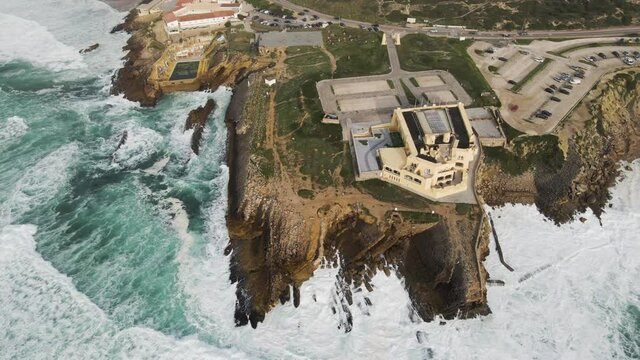 Aerial view of a desertic road driving next to a view of rough sea with crispy waves. Place situated in the south Portuguese wild coastline between the Atlantic ocean and the forest. Cascais, Portugal