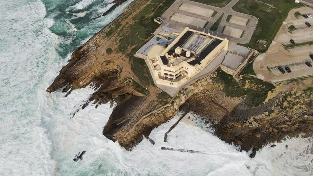 Aerial view of a desertic road driving next to a view of rough sea with crispy waves. Place situated in the south Portuguese wild coastline between the Atlantic ocean and the forest. Cascais, Portugal