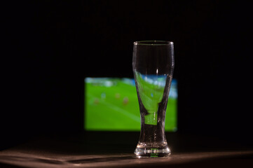 Empty beer glass and tv with football broadcast.