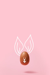 Minimalistic Easter background. A levitating chocolate egg with a rabbit face on a pink background. composition of an Easter greeting card.