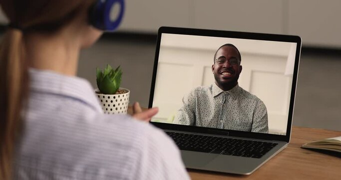 Back close up view young woman in headphones holding web camera zoom conversation with happy african american colleague, discussing working issues during virtual event, video call communication