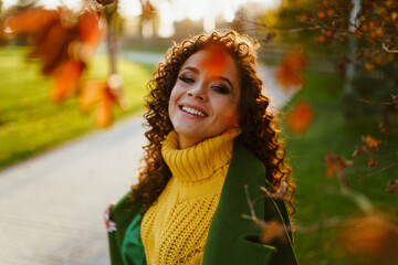 In the autumn park with yellow and crimson leaves there is a smiling beauty in a yellow sweater and...