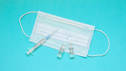 Syringe, ampoules with medicine and medical mask on blue background