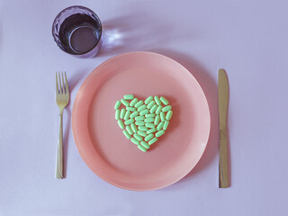 green tablets, vitamins in form of heart on the plate with glass of water on colorful background. Health care, treatment, food, cure concept