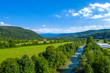 Fototapeta na wymiar Aerial view from drone of the vast green landscape with river, hills and blue sky