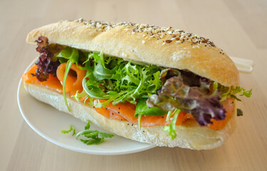 Baguette sub sandwich with smoke salmon fish, rocket lettuce, red oak lettuce on the table.