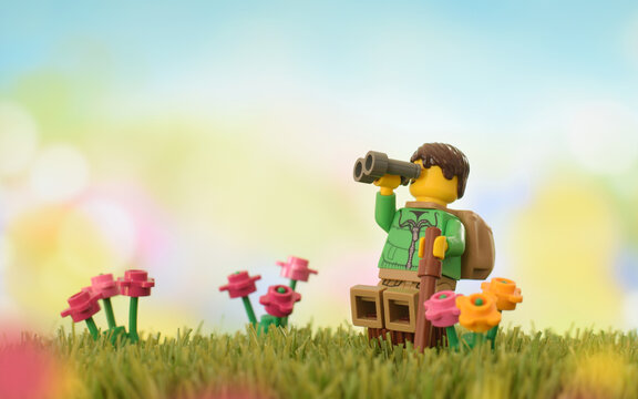 Lego minifigures happy cute boy with binocular on grass field or meadow at springtime. Editorial illustrative image of travel or vacation on nature.