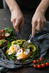 breakfast with poached egg on a slice of fried bread, avocado, arugula, cherry tomatoes and spices. Served in a cast-iron skillet, served with textiles on a black background