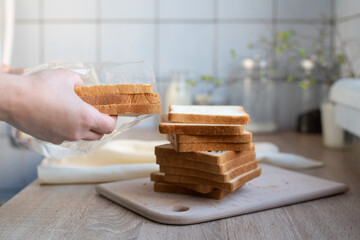 Female hands taking out slices of bread from a package on the kitchen table.
