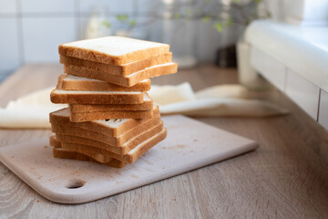 Tower of slices of toast bread on cutting board in the kitchen.